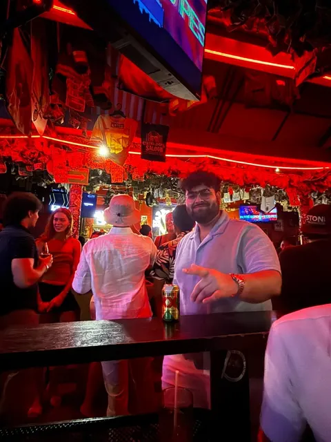 Karan at a neon-lit bar, mid gesture